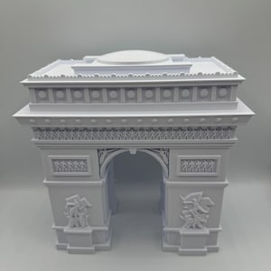 Może przedstawiać: Biała miniatura Łuku Triumfalnego. Model architektoniczny posiada szczeg&oacute;łowe rzeźbienia, w tym figury i elementy dekoracyjne. Łuk jest klasycznym zabytkiem.