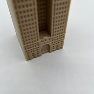 May include: A beige miniature building model with a detailed facade and a small entrance.