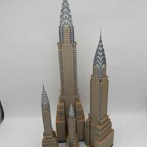 May include: A collection of five detailed miniature models of the Chrysler Building, featuring tan and silver color schemes. The models vary in size, showcasing the iconic Art Deco architecture. A wooden ruler is at the bottom.