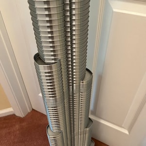 May include: A detailed model of a skyscraper, made of silver and grey plastic. The model is made up of many small, stacked pieces, creating a realistic representation of the building's design.