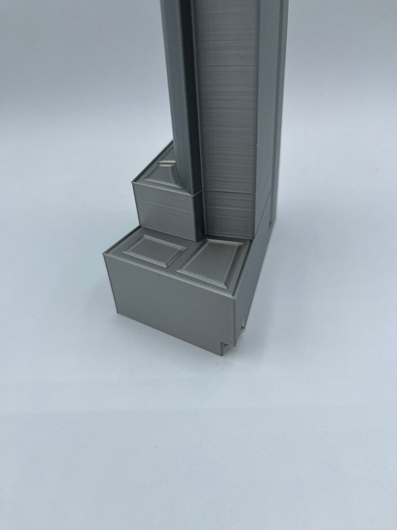 May include: A close-up of the base of a gray 3D printed model. The base is made up of several layers and has a textured surface.