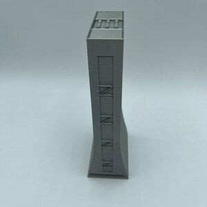 May include: A gray 3D printed model of a tall building with a flat roof and a series of windows on the front.