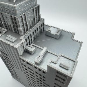 May include: A gray, 3D-printed model of a skyscraper with the word "EASTERN" printed on the side. The building has intricate architectural details, including windows, decorative elements, and a rooftop structure. The model is a detailed representation of a building.