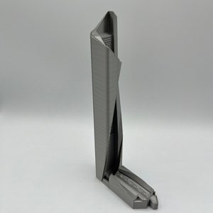 May include: A 3D printed model of a modern skyscraper with a unique, angular design. The model is made of gray plastic and has a detailed exterior.