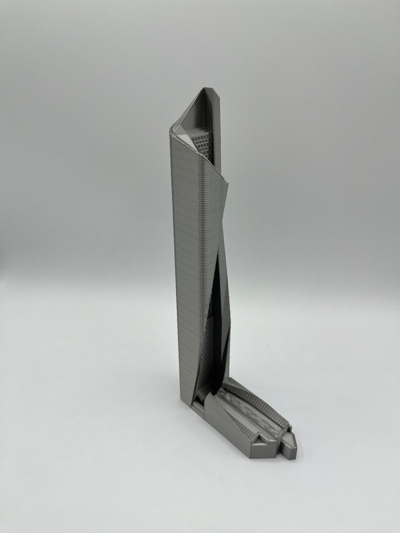 May include: A 3D printed model of a modern skyscraper with a unique, angular design. The model is made of gray plastic and has a detailed exterior.