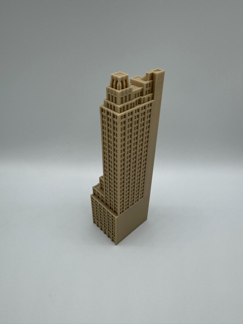 May include: A tan-colored, 3D-printed model of a skyscraper. The building has a stepped design with many windows and architectural details. The model is standing upright against a plain background.
