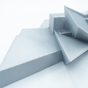 May include: A silver 3D printed abstract sculpture with geometric shapes and a textured surface.