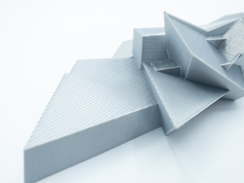 May include: A silver 3D printed abstract sculpture with geometric shapes and a textured surface.