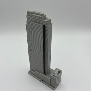 May include: A gray 3D printed model of a skyscraper with a rectangular base and a tall, narrow tower. The tower has a series of setbacks and a flat roof.