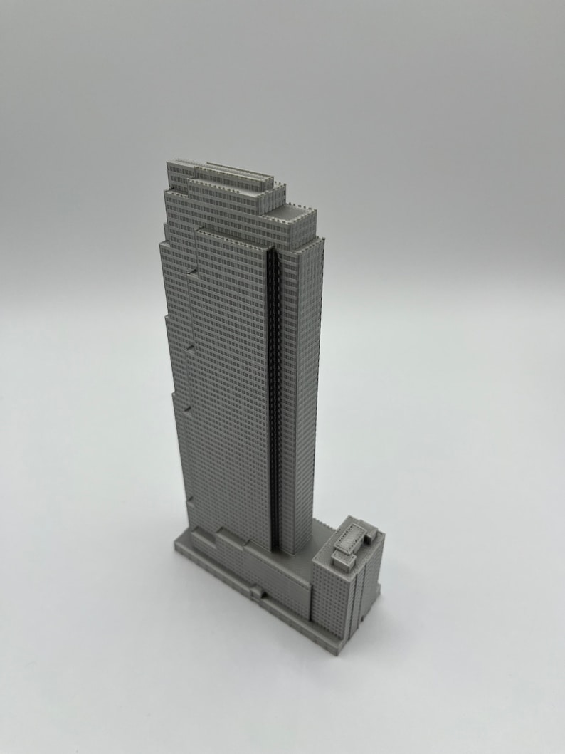 May include: A gray 3D printed model of a skyscraper with a rectangular base and a tall, narrow tower. The tower has a series of setbacks and a flat roof.