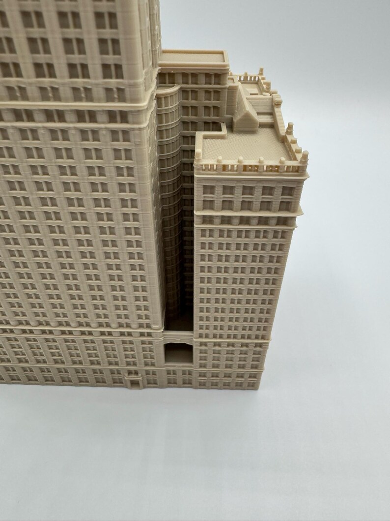 May include: A beige architectural model of a multi-story building with numerous windows. The building has a detailed facade and a recessed central section. The model is a detailed representation of a skyscraper.