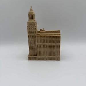 May include: A tan-colored architectural model of a tall building with a clock tower. The building has many windows and detailed architectural features. The model is set against a plain white background.