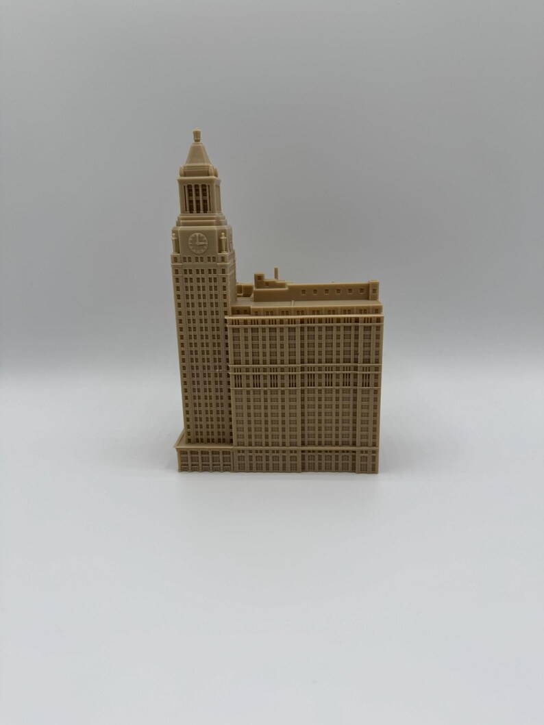 May include: A tan-colored architectural model of a tall building with a clock tower. The building has many windows and detailed architectural features. The model is set against a plain white background.