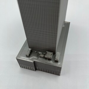 May include: A gray 3D printed model of a skyscraper with a detailed facade and a flat roof.