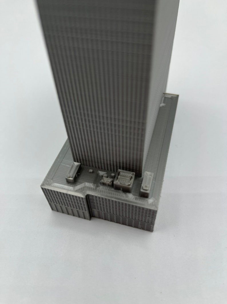 May include: A gray 3D printed model of a skyscraper with a detailed facade and a flat roof.