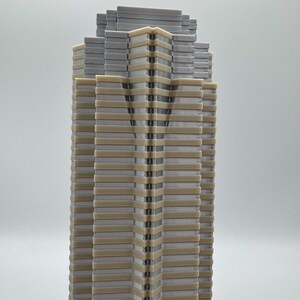 May include: A detailed model of a skyscraper, featuring a layered design with alternating gray and beige sections. The building's facade has a vertical pattern, and the top section has a stepped appearance. The model is set against a plain background.
