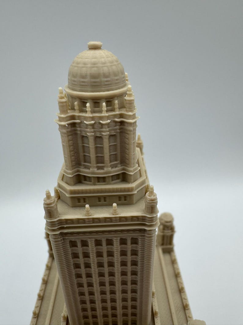 May include: A beige architectural model of a tall building with a domed top. The model has detailed windows and architectural features. The building's design includes multiple levels and decorative elements.