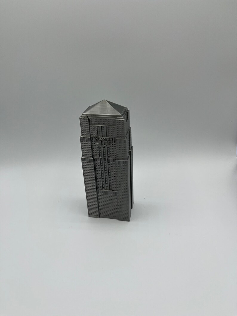 Peut inclure: Mod&egrave;le miniature d'un gratte-ciel avec une finition m&eacute;tallique grise. Le b&acirc;timent a un toit plat et une forme rectangulaire. Le b&acirc;timent a une petite enseigne qui indique "WAYNE" sur le devant.