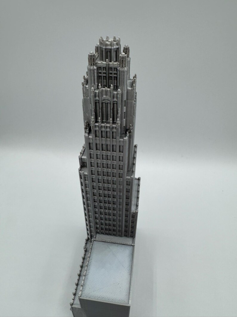 May include: A detailed, silver-colored model of a skyscraper. The building features a classic architectural design with numerous windows and intricate detailing on the upper levels. The model is a miniature representation of a tall building.