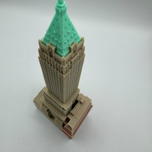 May include: A 3D printed model of a skyscraper with a green roof and brown walls. The model is detailed with windows and a base.