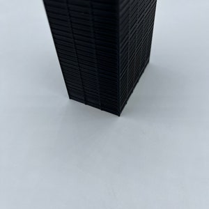 May include: A black, rectangular, 3D printed model of a skyscraper.