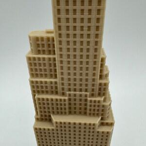 May include: A beige 3D printed model of a skyscraper with a detailed facade. The model is made of plastic and has a smooth finish.