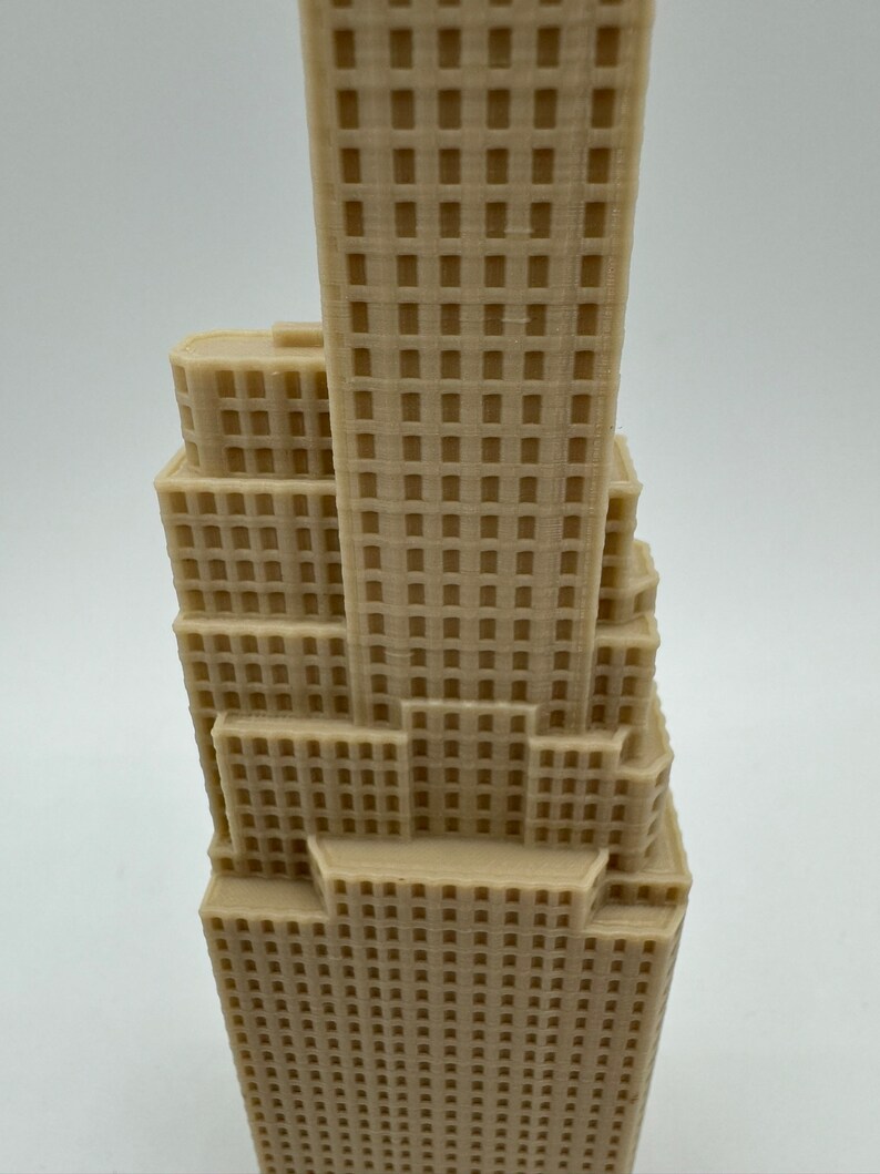 May include: A beige 3D printed model of a skyscraper with a detailed facade. The model is made of plastic and has a smooth finish.