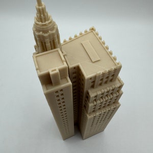 Pu&ograve; includere: Un modello di grattacielo stampato in 3D di colore beige con un tetto a punta e una facciata dettagliata.
