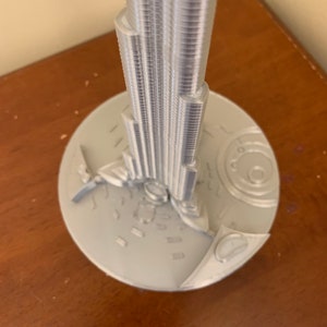 May include: A silver model of the Burj Khalifa, a skyscraper in Dubai, with a detailed base.