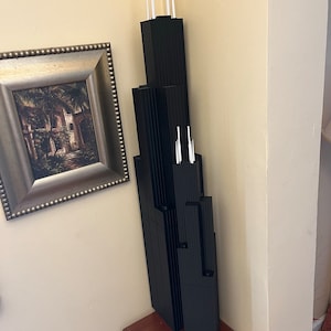 May include: A black model of the Willis Tower, formerly known as the Sears Tower, with white spires on top. The model is sitting on a wooden table.