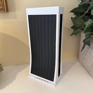 May include: A white and black model of a skyscraper with a curved design. The model is made of cardboard and has a black grid pattern on the front.