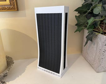 May include: A white and black model of a skyscraper with a curved design. The model is made of cardboard and has a black grid pattern on the front.