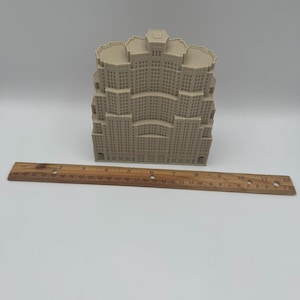 May include: A beige architectural model of a skyscraper with multiple tiers and windows. A wooden ruler with centimetre markings is placed in front of the model, measuring approximately 30 cm.
