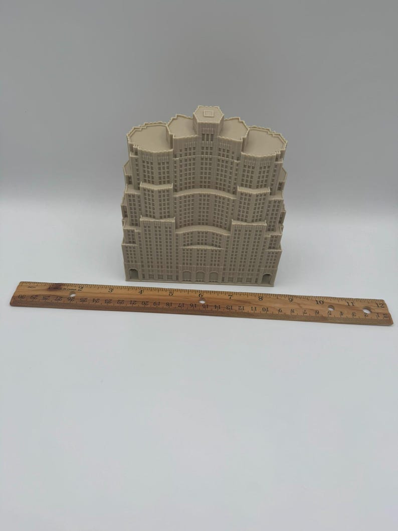 May include: A beige architectural model of a skyscraper with multiple tiers and windows. A wooden ruler with centimetre markings is placed in front of the model, measuring approximately 30 cm.