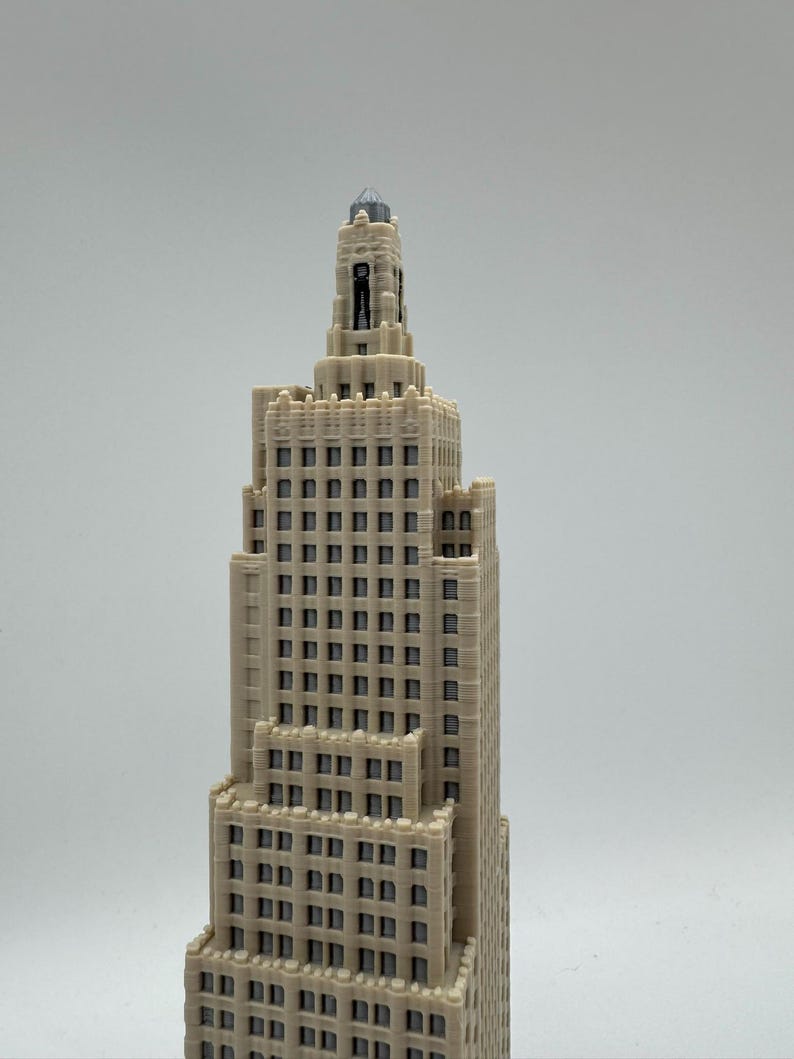 May include: A detailed miniature model of a beige skyscraper with a tiered design. The building features numerous windows and architectural details, with a spire at the top. The model is set against a plain background.