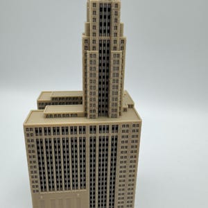 May include: A beige architectural model of a skyscraper with a tiered design. The building has numerous windows and a green-roofed top. The model is set against a plain white background.