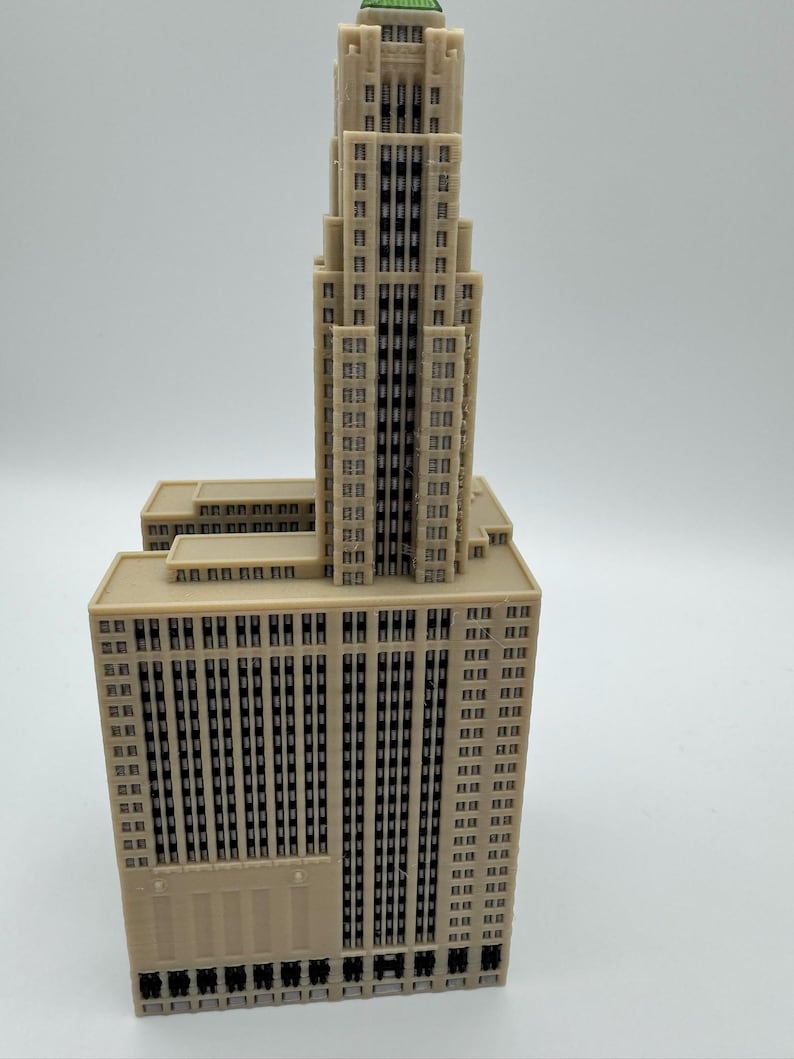 May include: A beige architectural model of a skyscraper with a tiered design. The building has numerous windows and a green-roofed top. The model is set against a plain white background.