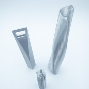 May include: Three silver 3D printed models of skyscrapers. The tallest model is a twisted tower, the middle model is a rectangular tower with a window, and the shortest model is a square tower with a pointed top.