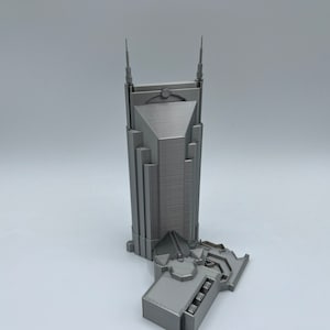 May include: A 3D printed model of a skyscraper with a gray finish. The building has a pointed roof and a base with a detailed design.