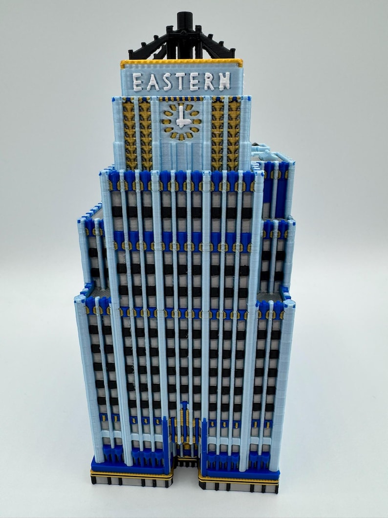 May include: A light blue model of a building with the word "EASTERN" on top. The building has a clock and gold and blue accents. The windows are black and the building is on a white surface.
