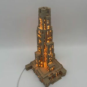 May include: A beige, multi-tiered architectural model of a skyscraper featuring a vertical design with numerous rectangular windows. The structure is illuminated from within, casting a warm, glowing orange light through the window openings.