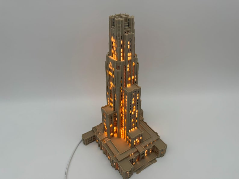 May include: A beige, multi-tiered architectural model of a skyscraper featuring a vertical design with numerous rectangular windows. The structure is illuminated from within, casting a warm, glowing orange light through the window openings.
