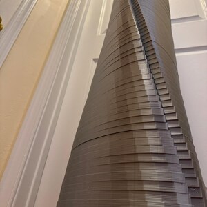 May include: A tall, grey, 3D printed sculpture resembling a tower or building. The sculpture is made of many stacked layers, creating a spiral effect.