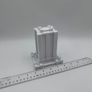 May include: A white 3D printed model of a tall building with a crenellated roof and a base with a decorative design. The model is approximately 6 inches tall and is sitting on a white surface.