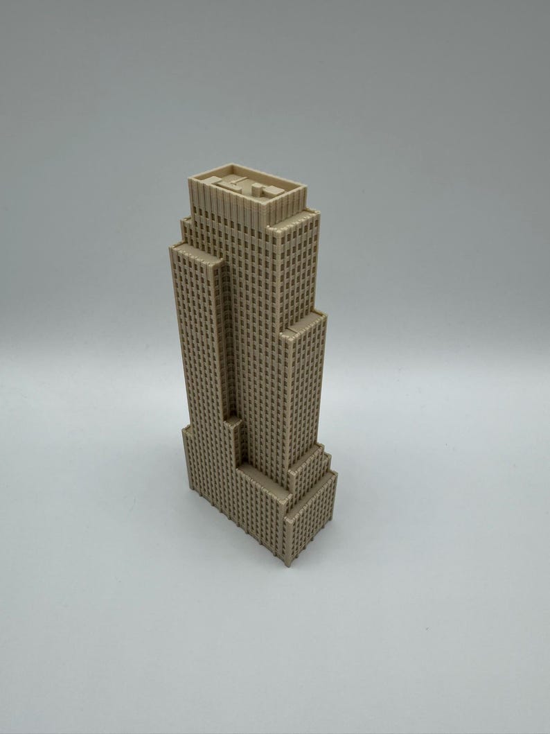 May include: A beige-colored miniature skyscraper model with a multi-tiered design. The building has numerous small, square windows and a flat roof. The model is a detailed representation of a tall building.