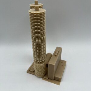 May include: A 3D printed model of a beige skyscraper with a unique, geometric design. The building has a tall, cylindrical tower with a series of stacked, circular elements. The model is detailed and realistic, capturing the architectural features of the original building.