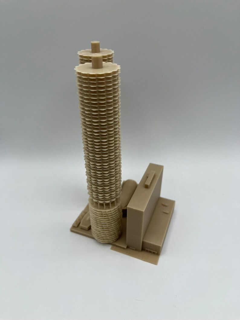 May include: A 3D printed model of a beige skyscraper with a unique, geometric design. The building has a tall, cylindrical tower with a series of stacked, circular elements. The model is detailed and realistic, capturing the architectural features of the original building.