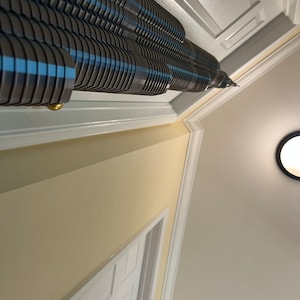 May include: A close-up view of a ceiling-mounted window blind with a unique design. The blind is made of a series of overlapping, horizontal slats that are alternating shades of grey and blue. The slats are arranged in a staggered pattern, creating a visually interesting effect.