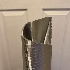 May include: A silver metal 3D printed model of a tall building with a curved top.