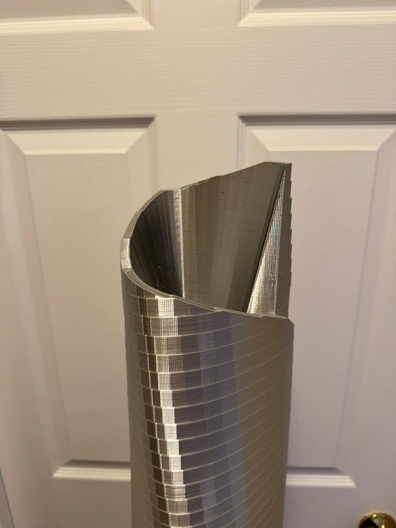 May include: A silver metal 3D printed model of a tall building with a curved top.